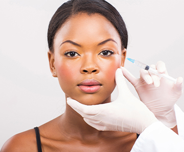 Cosmetic surgeon injecting young African woman's face